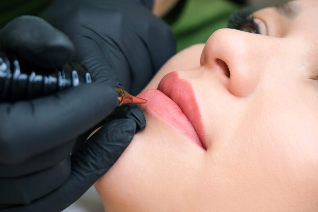 Young woman having permanent makeup on her lips at the beauticians salon. Natural green background